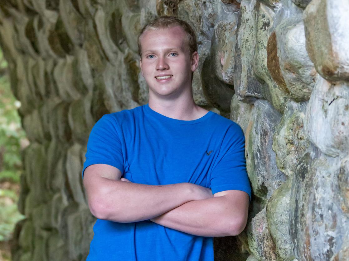 Ethan Rhodig wearing a blue shirt leaning against a rock wall